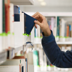 hand pulling a book off of a library shelf