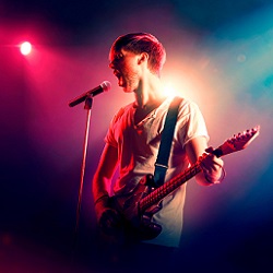 male singer playing guitar under stage spotlight