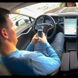man in driver's seat of autonomous vehicle looks at cellphone