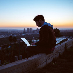 man with a laptop computer sitting on a wall