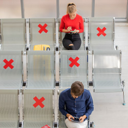 passengers in airport terminal separated by seats marked 'x'