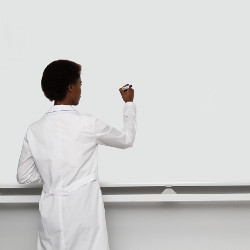 black woman in white coat writing on white blackboard