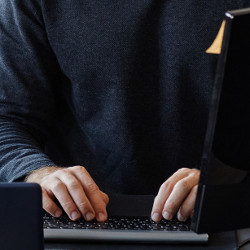 hands of a man in a dark sweater on a computer keyboard