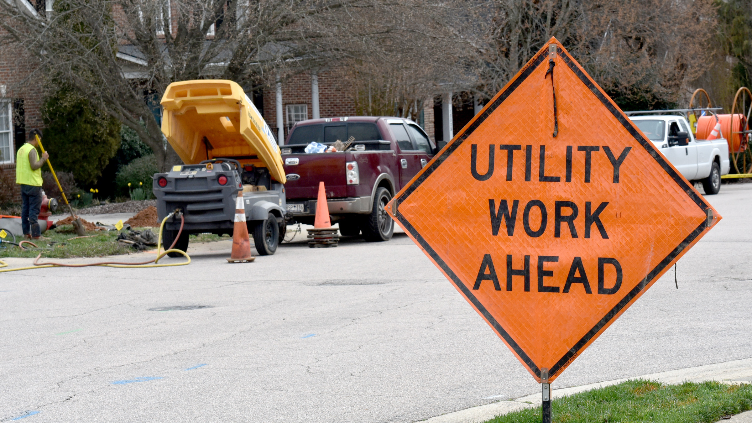 worker with shovel on a street with a road sign stating 'Utility Work Ahead'